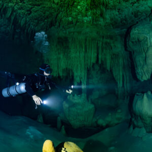 Sidemount diver with torch facing a green stalactite curtain, Quintana Roo, Mexico