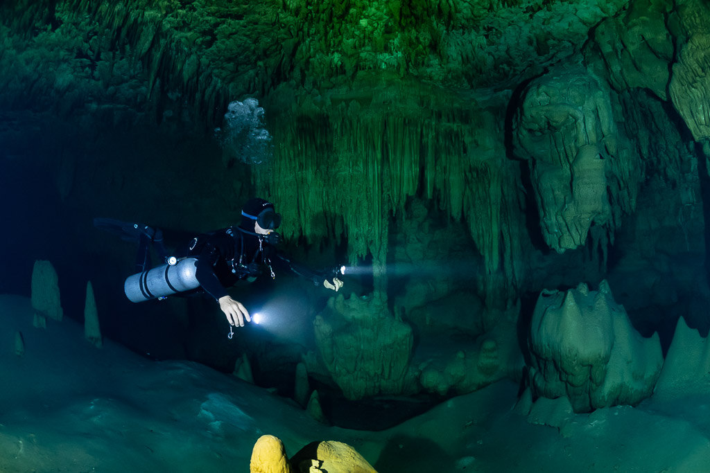 Plongeur en sidemount face à un rideau de stalactites vert, lampe allumée, Quintana Roo, Mexique