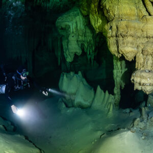 Sidemount diver with two lights near cone-shaped stalagmites, Quintana Roo, Mexico