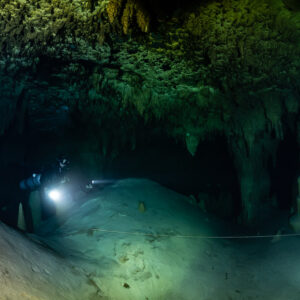 Distant diver with torch on a pale mound in a dark chamber, Quintana Roo, Mexico