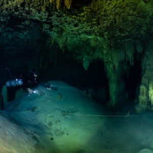 Diver crossing a pale mound under a decorated ceiling, lit column, Quintana Roo, Mexico