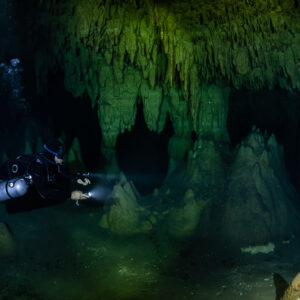 Sidemount diver lighting conical stalagmites below hanging draperies, Quintana Roo, Mexico