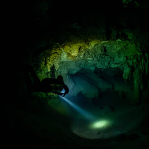 Diver beaming torch onto the floor in near-total darkness, Quintana Roo, Mexico