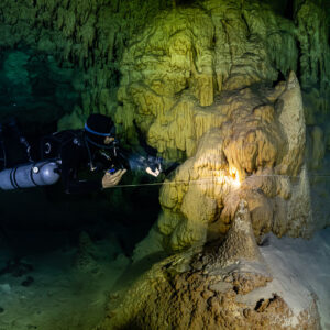 Sidemount diver lighting a large golden stalagmite mound, Quintana Roo, Mexico