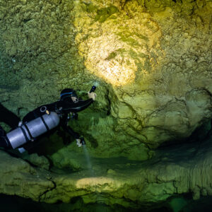 Sidemount diver lighting a hollow in a golden flowstone wall, Quintana Roo, Mexico