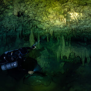 Sidemount diver holding two torches below green stalactites, Quintana Roo, Mexico