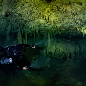 Sidemount diver lighting the ceiling under green stalactites, Quintana Roo, Mexico