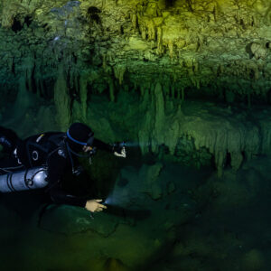 Sidemount diver close-up beaming forward under green stalactites, Quintana Roo, Mexico