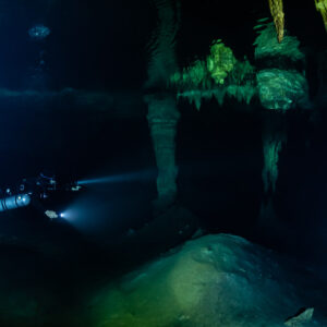 Sidemount diver below a long stalactite in deep blue darkness, Quintana Roo, Mexico