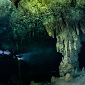 Sidemount diver beaming toward a massive stalactite column, Quintana Roo, Mexico