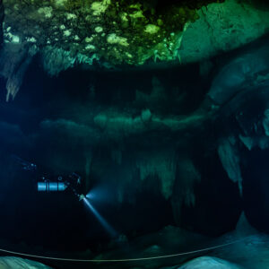 Sidemount diver beaming torch under a broad green limestone ceiling, Quintana Roo, Mexico