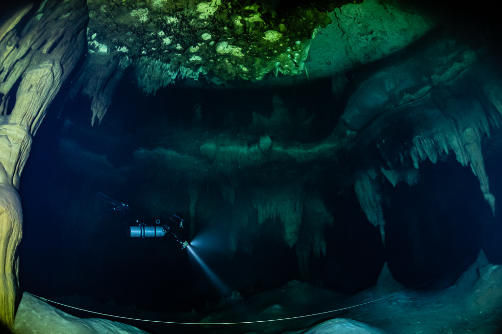 Plongeur en sidemount éclairant sous un large plafond calcaire vert, Quintana Roo, Mexique