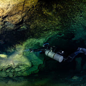 Sidemount diver lighting a low golden wall near a passage, Quintana Roo, Mexico