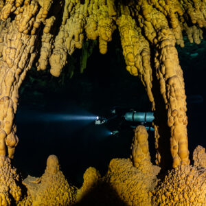 Distant diver framed by orange stalactite columns, Quintana Roo, Mexico