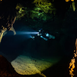 Diver beaming torch beyond orange columns and stalagmites, Quintana Roo, Mexico