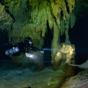Sidemount diver beaming past golden columns, closer framing, Quintana Roo, Mexico