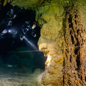 Two divers with torches beside a massive orange column, Quintana Roo, Mexico