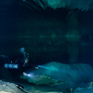 Sidemount diver lighting a pale boulder in deep blue water, Quintana Roo, Mexico