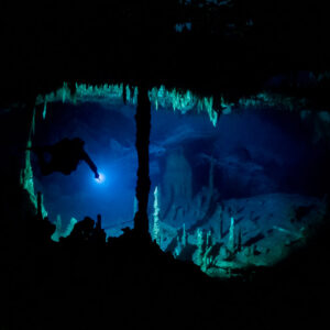 Cave diver silhouetted in a window of blue light framed by formations, Quintana Roo, Mexico