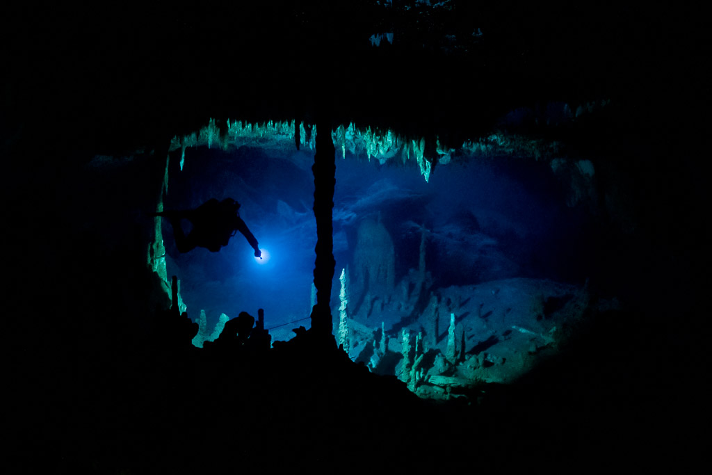 Plongeur spéléo en silhouette dans une fenêtre de lumière bleue encadrée de concrétions, Quintana Roo, Mexique