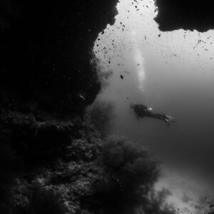 Black and white woman diver beyond a reef cave opening, Maaya Thila, Maldives