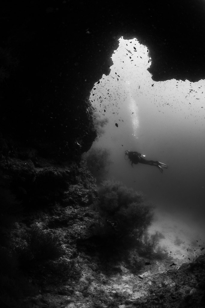 Black and white woman diver beyond a reef cave opening, Maaya Thila, Maldives