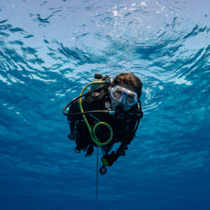 Woman diver ascending toward the camera under the rippled surface, Devana Kandu, Maldives