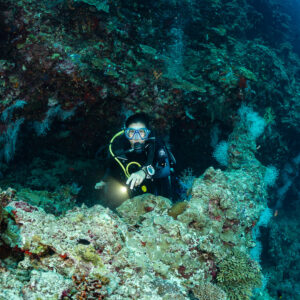 Woman diver with torch emerging from a reef crevice, Kuda Giri Wreck, Maldives