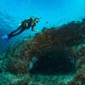 Woman diver swimming above a reef arch under blue water, Kuda Giri Wreck, Maldives