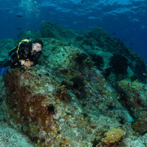 Diver peeking over a large rock, looking at camera, Komodo, Indonesia