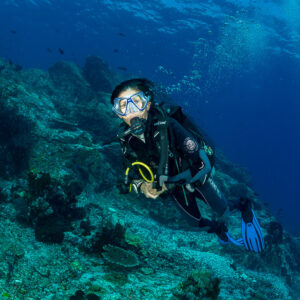 Diver facing the camera in close-up beside a rocky slope, Komodo, Indonesia