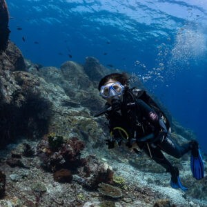 Diver swimming toward the camera beside a rock wall, bubbles rising, Komodo, Indonesia