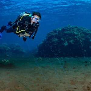 Woman diver above sandy bottom with gas bubbles near coral mound, Sangeang Island, West Nusa Tenggara, Indonesia