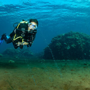 Woman diver facing camera over sand seeping volcanic gas bubbles, Sangeang Island, West Nusa Tenggara, Indonesia