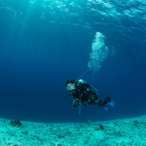 Woman diver with exhaled bubbles over sand in deep blue water, Komodo, Indonesia