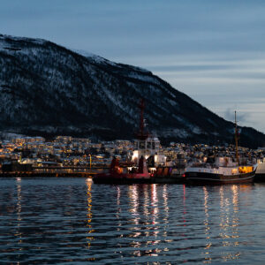 Harbour at dusk with moored boats and city lights below a dark mountain, Tromsø, Troms, Norway