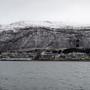 Ville étirée le long du rivage sous une montagne enneigée et un ciel gris, Tromsø, Troms, Norvège