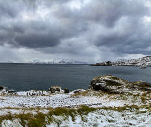Panorama of a snowy fjord shore with red cabins under dramatic clouds, Seglvik, Troms, Norway