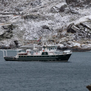 Expedition vessel anchored below snowy rocky slopes in a dark fjord, Seglvik, Troms, Norway