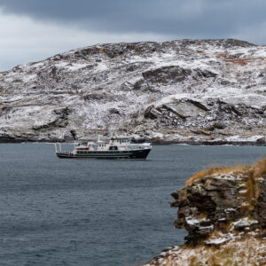 Small expedition ship in a fjord framed by snowy hills and a rocky point, Seglvik, Troms, Norway