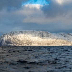 Chaîne de montagnes enneigées ensoleillée au-delà des eaux sombres et agitées du fjord, Kvænangen, Troms, Norvège