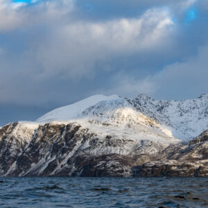 Snow-dusted mountains under billowing clouds seen from the fjord surface, Kvænangen, Troms, Norway