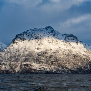 Pyramid-shaped snowy peak lit by low sun above the fjord, Kvænangen, Troms, Norway