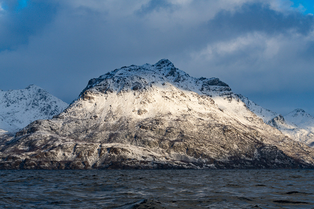 Sommet enneigé en forme de pyramide éclairé par le soleil rasant au-dessus du fjord, Kvænangen, Troms, Norvège