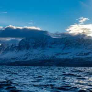Long snowy mountain ridge under blue sky and a bank of clouds, Kvænangen, Troms, Norway