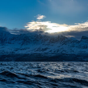 Backlit cloud above a blue snowy mountain ridge and rough fjord water, Kvænangen, Troms, Norway