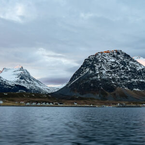 Snow-capped peaks above a small shoreline village seen from the fjord, Kvænangen, Troms, Norway