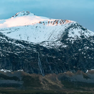 Snowy summit and cliff with waterfall over the fjord shore, vertical frame, Kvænangen, Troms, Norway