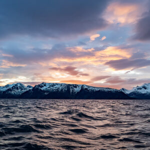 Chaîne enneigée sous des nuages colorés du crépuscule sur un fjord agité, Kvænangen, Troms, Norvège