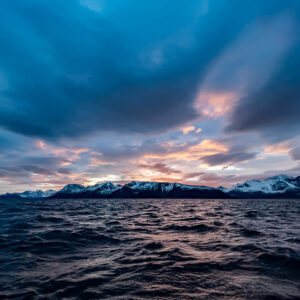 Blue dusk sky with streaks of orange over snowy mountains and fjord, Kvænangen, Troms, Norway